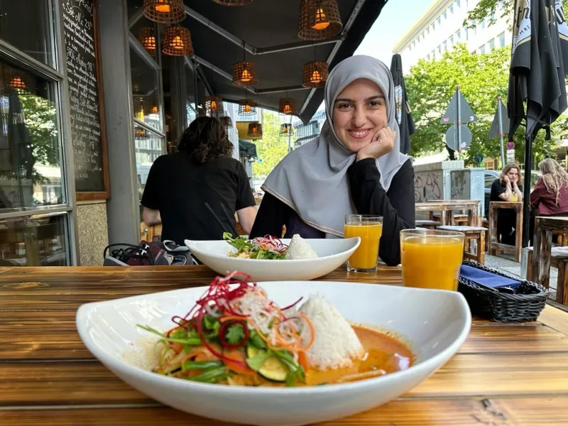 A young woman is sitting at a restaurant table. On the table there are two plates filled with rice and vegetable dishes.