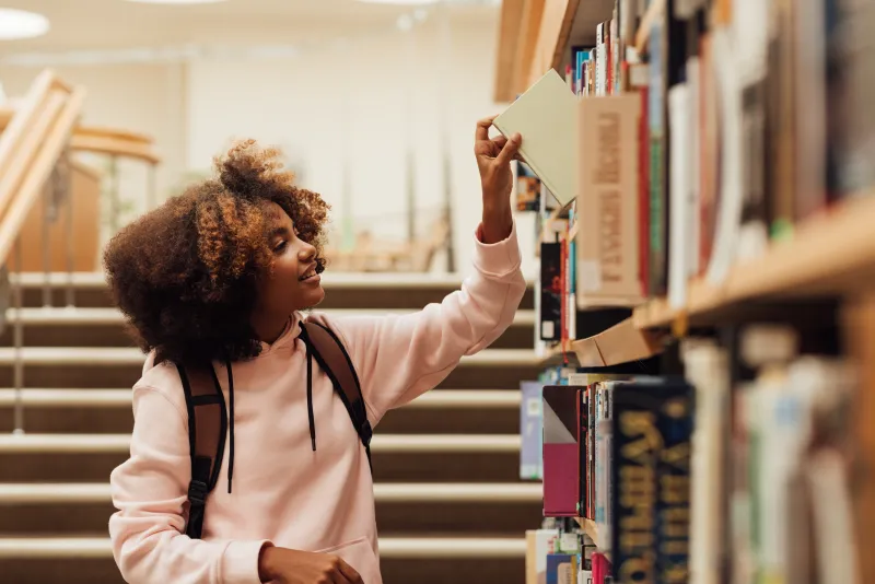 Woman_Taking_A_Book_From_Bookshelf_In_Library