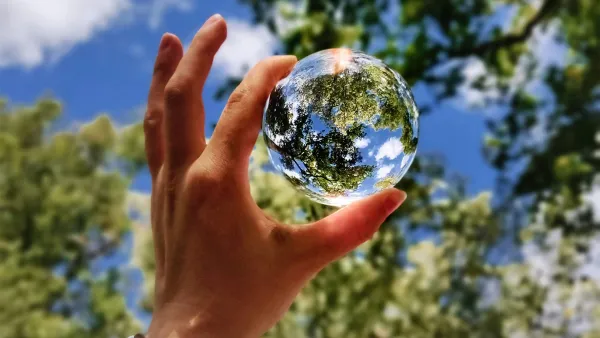 A hand holding a glass ball against a blue sky and green leaves
