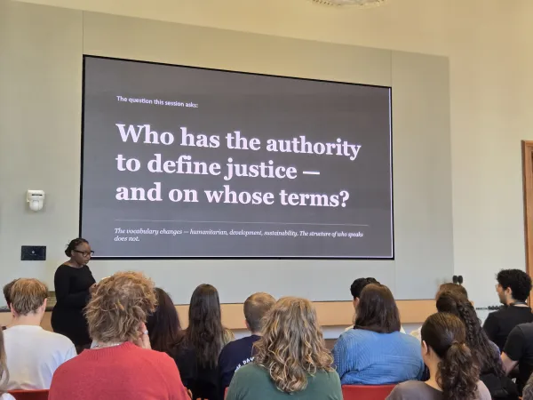 A lecture during the "Circle U.nited for Sustainability" summer school. Students looking at a slide that reads "Who has the authority to define justice - and on whose terms?".