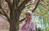 A smiling woman is standing beneath a cherry blossom tree. 